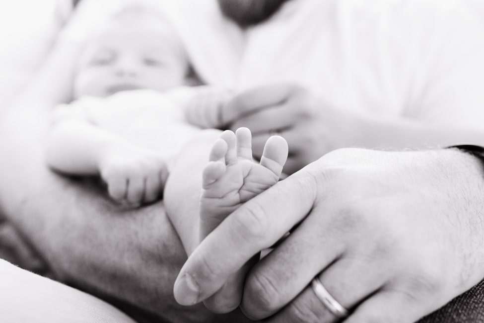 a black and white photo of a man holding a baby's foot.
