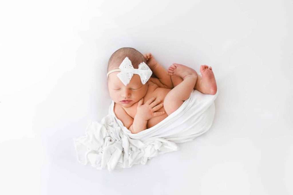 A newborn girl captured by a Phoenix maternity photographer, wrapped in a white blanket against a seamless white background.