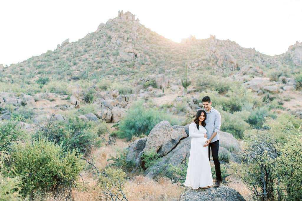 A couple on rocks in the desert during their Arizona maternity session, photographed by a maternity photographer in Phoenix.