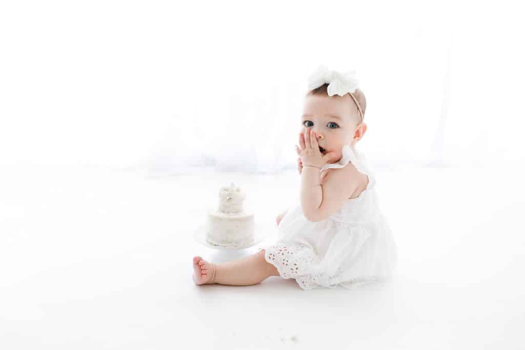 A newborn baby girl in front of a white cake, captured by a family photographer in Phoenix.