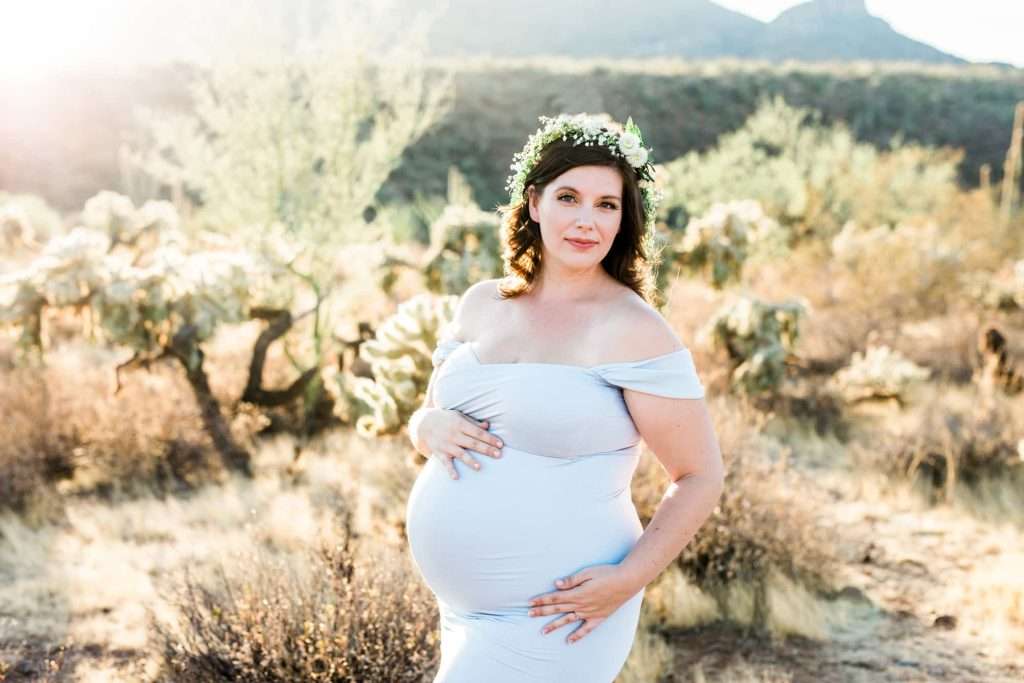 A pregnant woman in a white dress standing in the Phoenix desert.