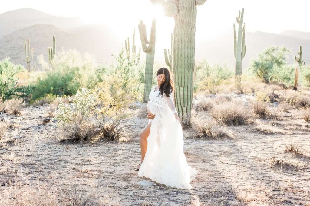 A Phoenix woman in a white dress standing in front of a cactus, captured by a photographer.