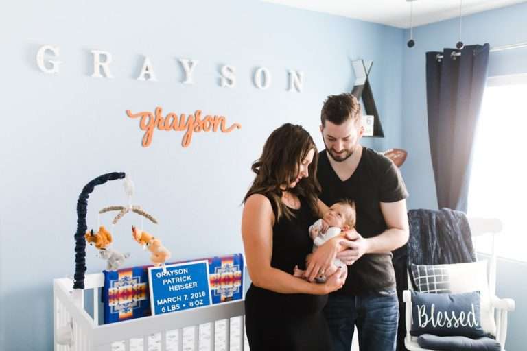 Lifestyle newborn photography capturing a man and woman holding a baby in a blue nursery.