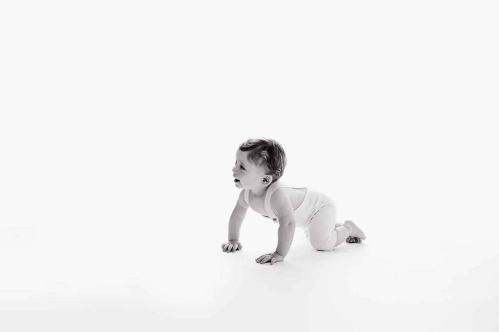 a black and white photo of a baby crawling on the floor during a cake smash photoshoot.