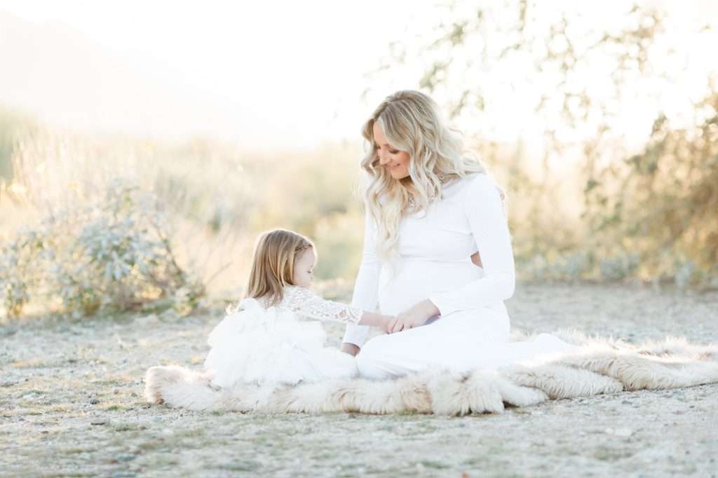 A woman in a white dress poses with her daughter for a family photographer in Phoenix.