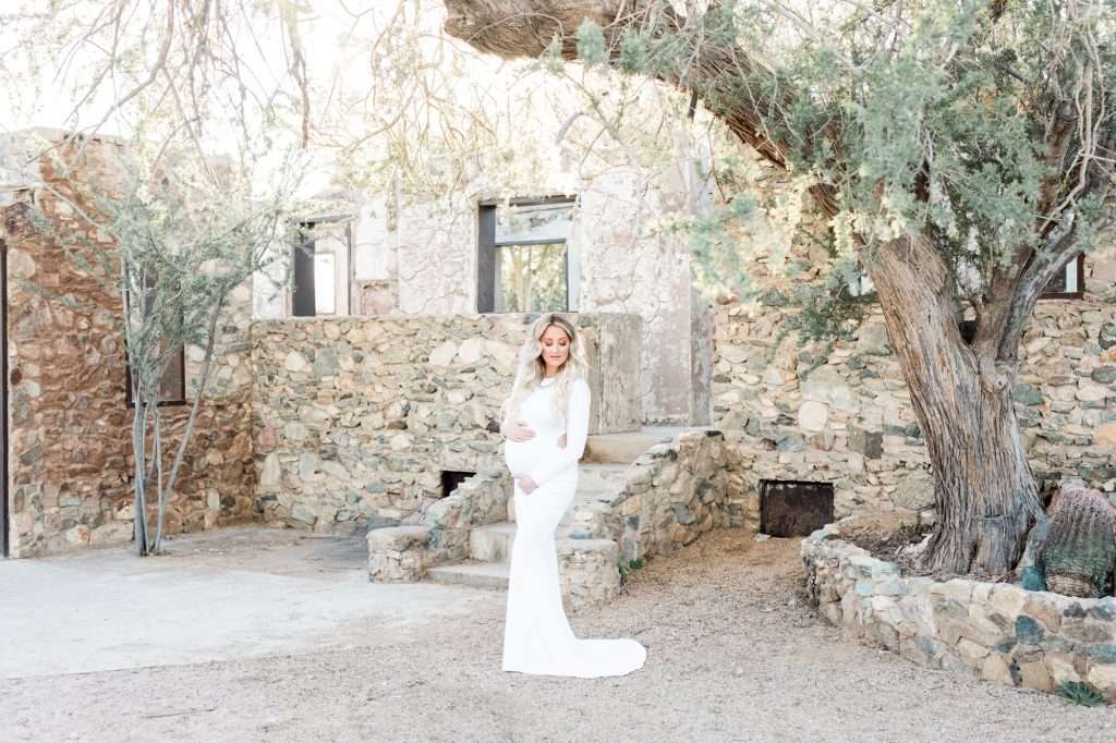 A bride in a white dress standing in front of a stone house, captured by a family photographer in Phoenix.