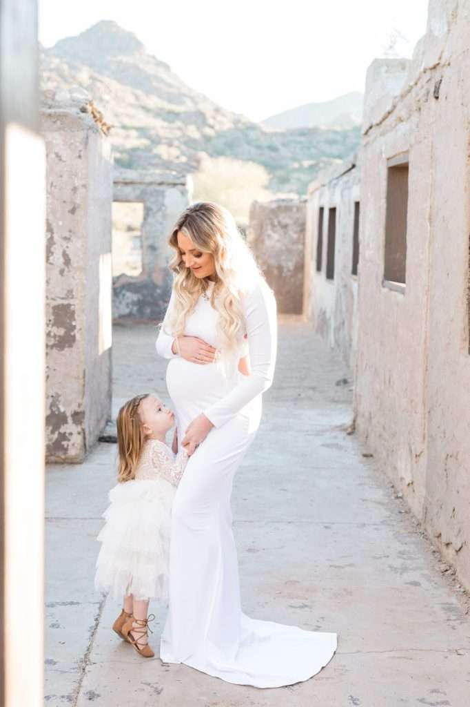 A family photographer capturing a pregnant woman and her daughter in an alleyway.