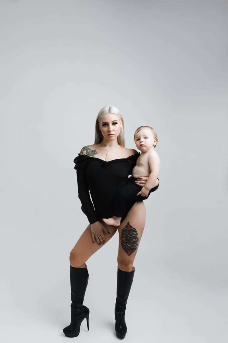 A woman in black holding her baby, captured in a photo studio by a family photographer specializing in newborn photography.