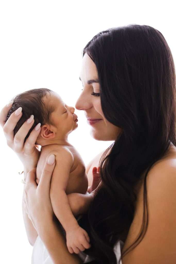 Newborn Photography: A woman embracing her newborn baby against a white background.