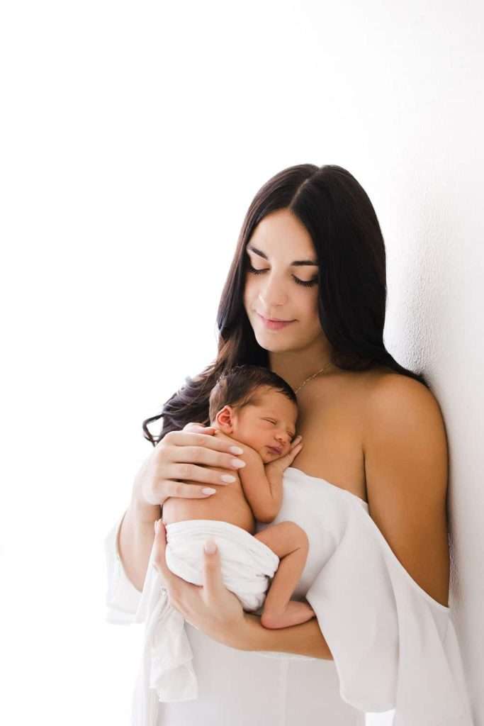 A woman holding her newborn baby in front of a white wall.
