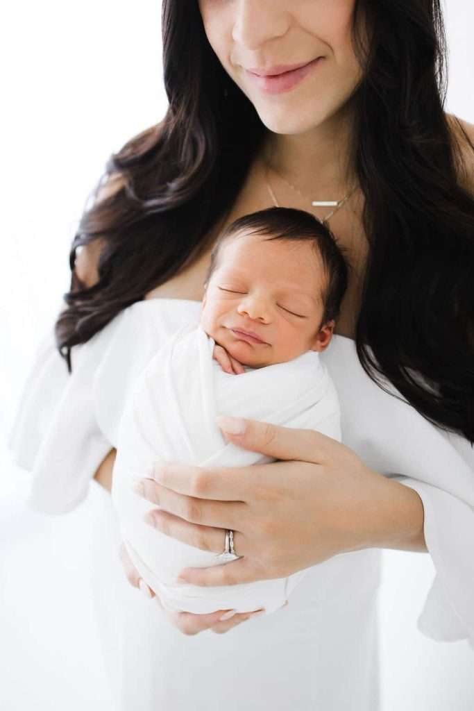 Newborn Photography of a woman holding a baby wrapped in a white blanket.
