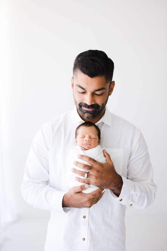 A man capturing newborn photography with a baby in his arms.