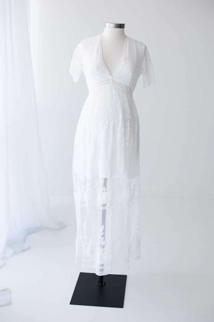 A white, short-sleeved, V-neck sheer dress with lace details displayed on a dress form against a plain white background.