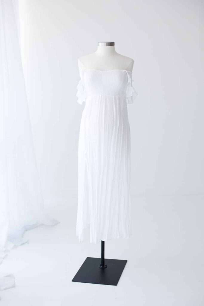 A white off-the-shoulder, ankle-length dress displayed on a dress form against a plain white background.