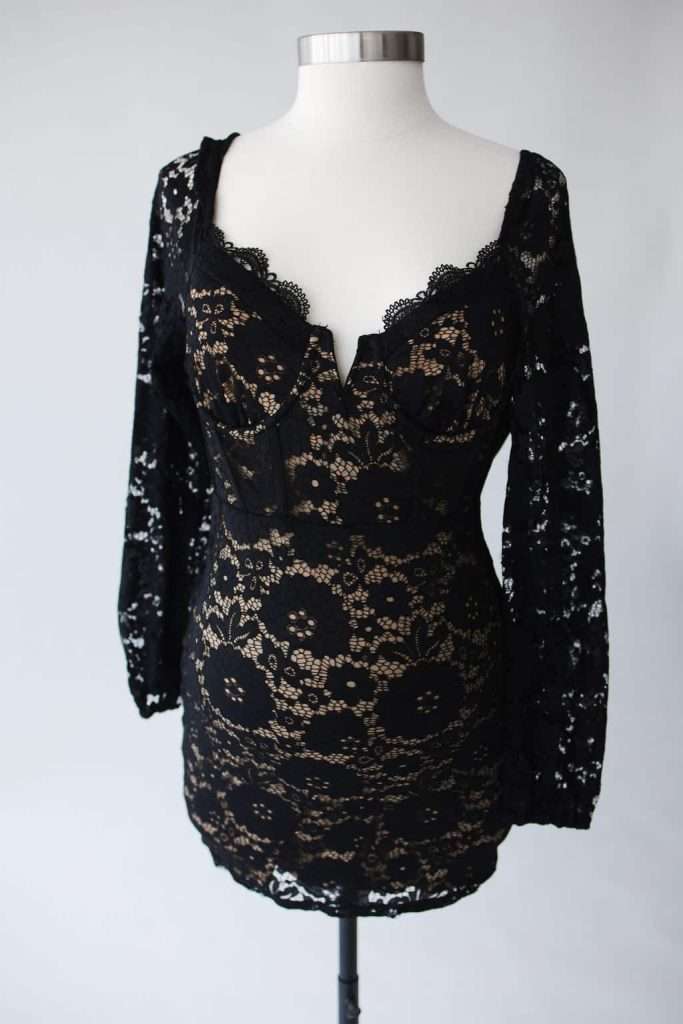 Black lace long-sleeve mini dress with a deep neckline and nude lining displayed on a dress form against a plain background.