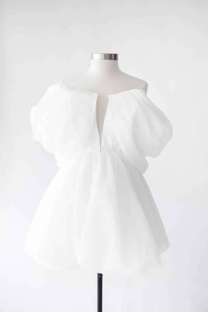 A white, short, off-the-shoulder dress with voluminous puff sleeves displayed on a dress form against a plain background.