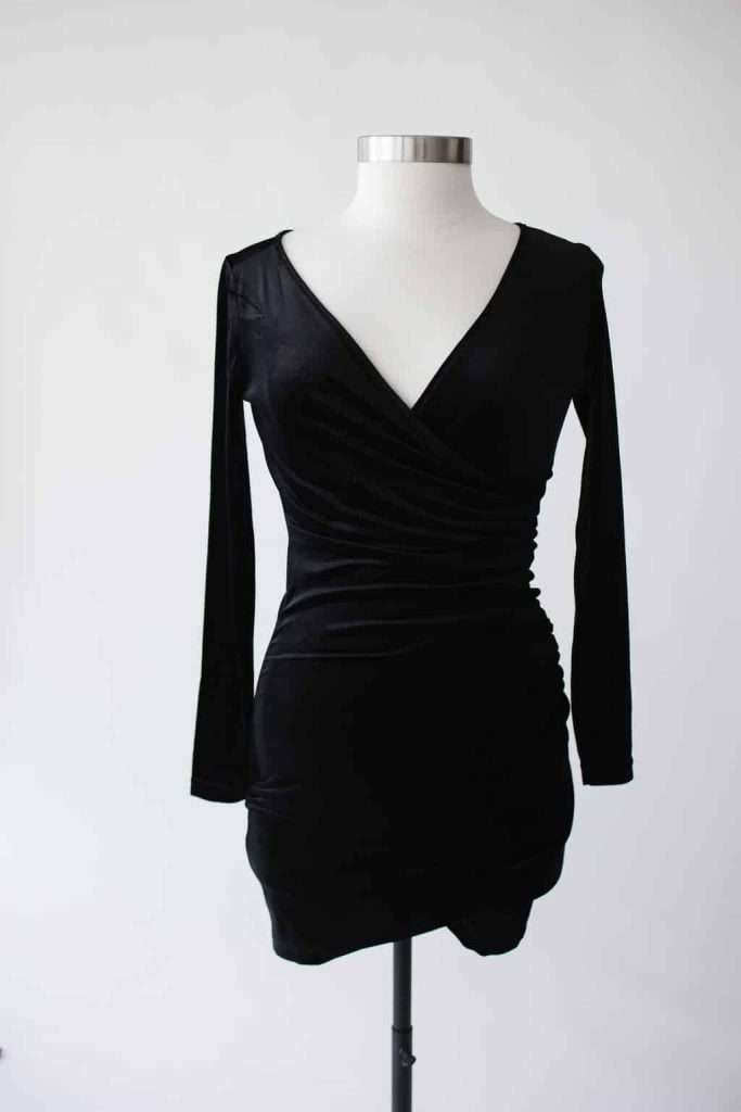 Black, long-sleeved, V-neck, wrap-style mini dress displayed on a dress form against a plain white background.