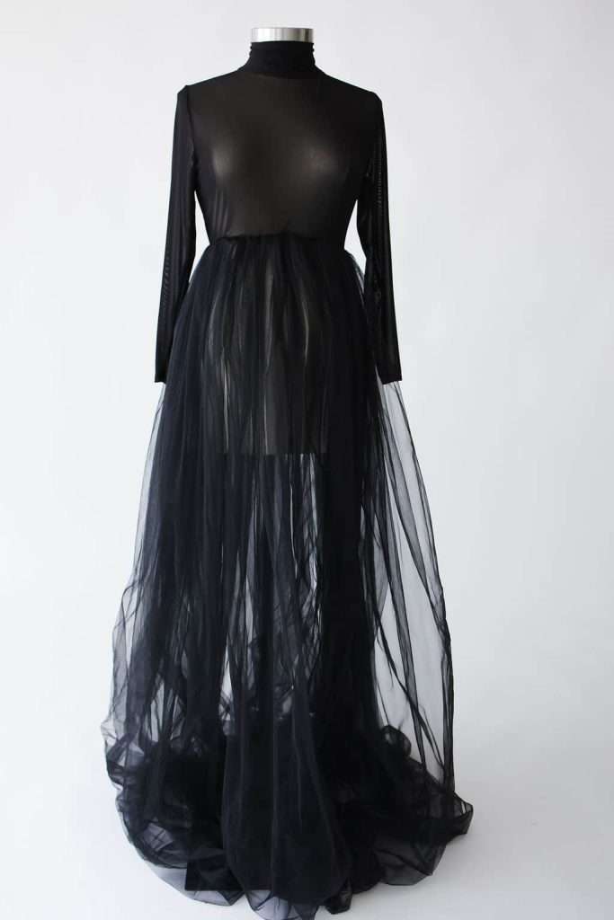 Black sheer long-sleeve gown with a fitted bodice and high neckline, featuring a flowing, transparent tulle skirt. Displayed on a mannequin against a plain background.