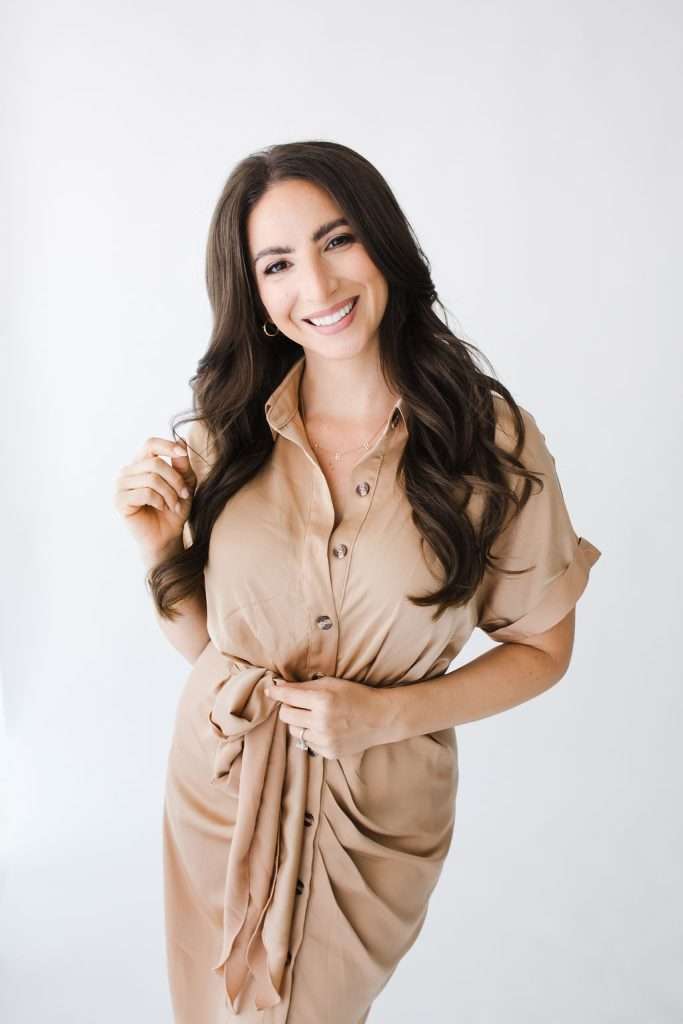 Woman with long brown hair wearing a tan button-down dress stands smiling against a plain white background, perfect for a Family Photographer Phoenix portfolio.