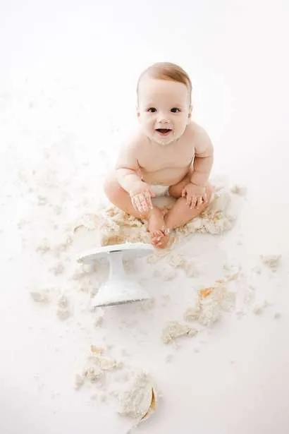 A baby sits on the floor surrounded by cake crumbs, with an overturned cake stand nearby—captured candidly by a Family Photographer in Phoenix.