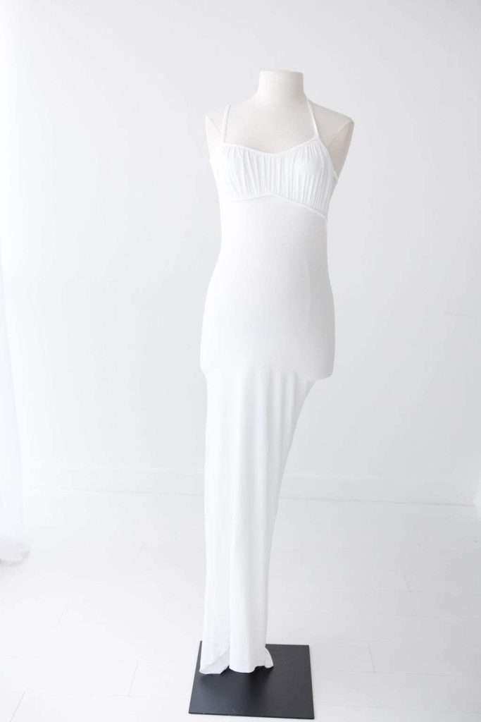 A white, floor-length, sleeveless dress with a halter neckline is displayed on a plain dress form against a white background.