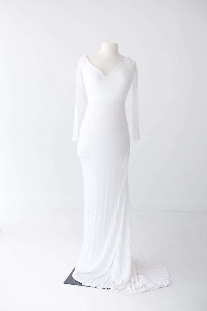 A long-sleeved, floor-length white gown with a V-neckline is displayed on a mannequin against a plain white background.