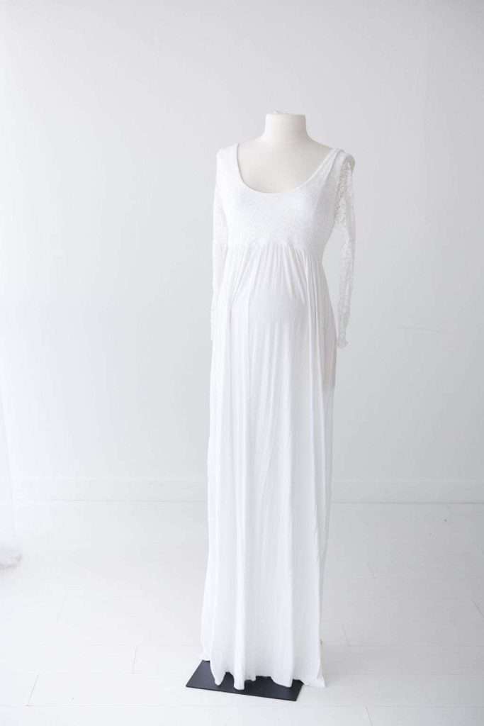 A white, long-sleeved, floor-length maternity dress displayed on a headless mannequin against a plain white background.