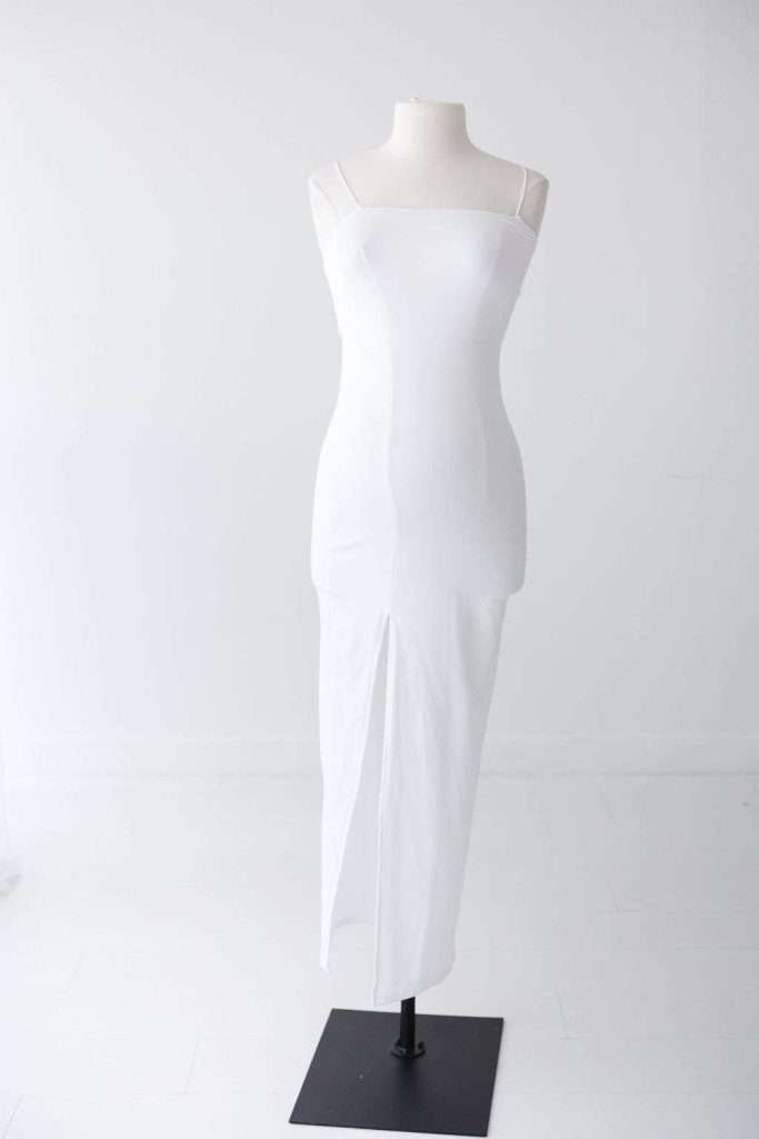 A white sleeveless dress with thin straps and a front slit displayed on a mannequin against a plain white background.