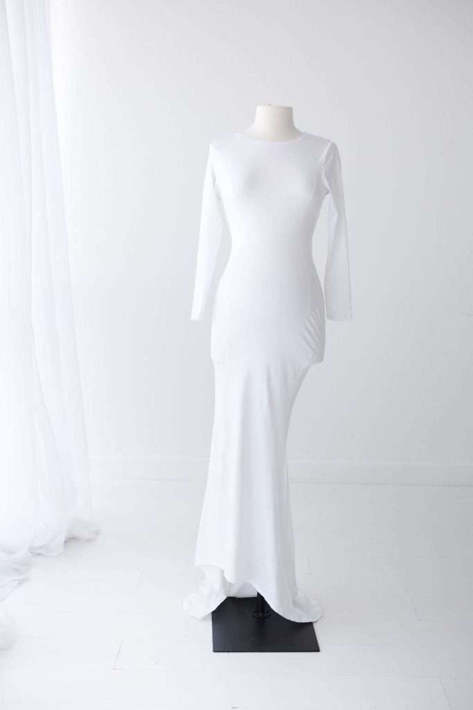 A white, long-sleeved, floor-length gown is displayed on a mannequin in a minimalistic, white room.