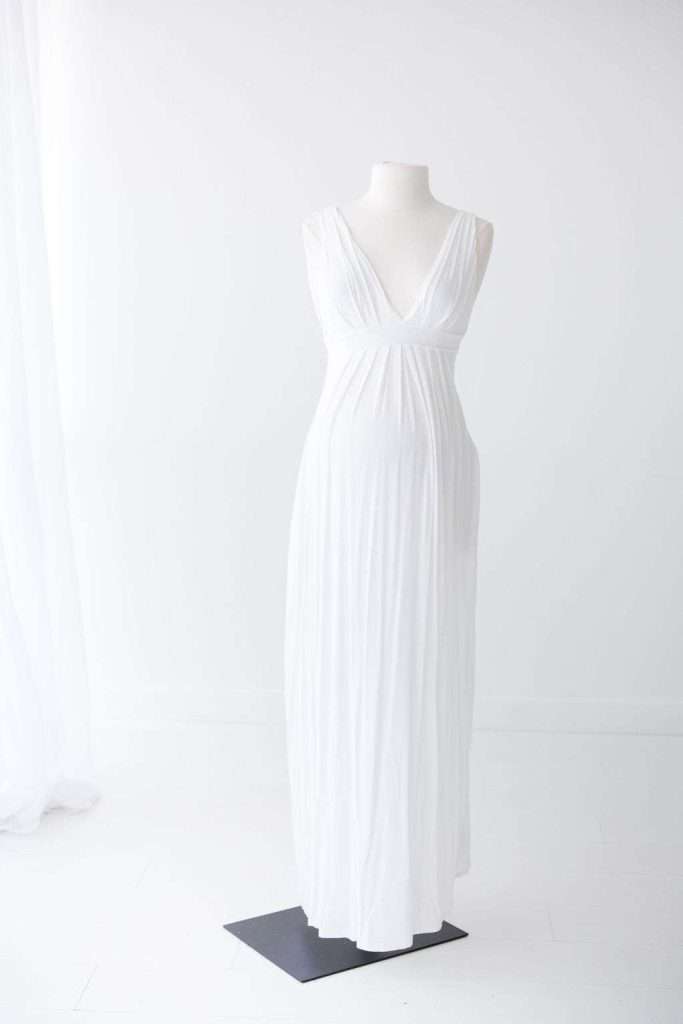 A white, sleeveless, floor-length dress with a deep V-neck displayed on a headless mannequin against a plain white background.