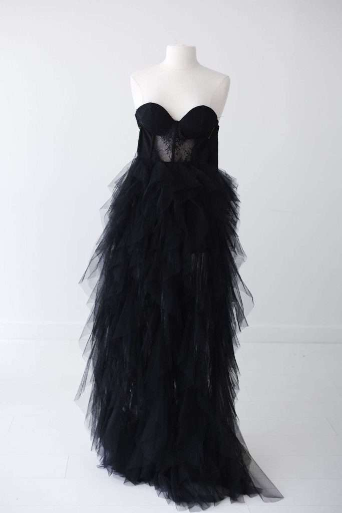 A strapless black dress with a fitted bodice and a voluminous layered tulle skirt, displayed on a white mannequin in a minimalist setting.