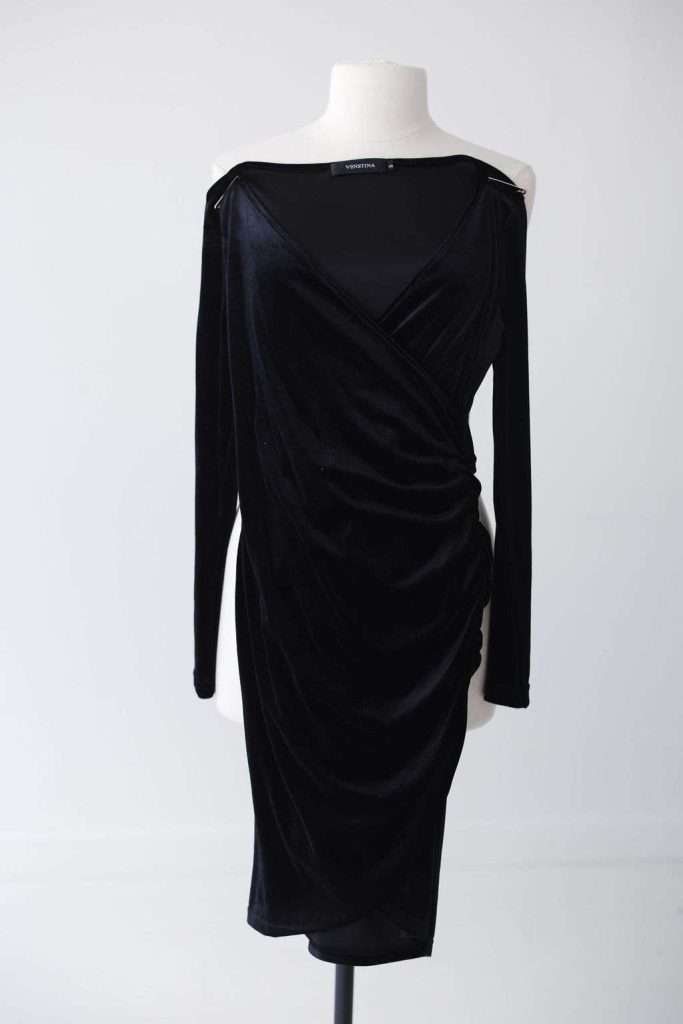 Black velvet long-sleeve dress on a white mannequin, featuring a V-neckline and ruched side detailing, displayed against a plain light background.