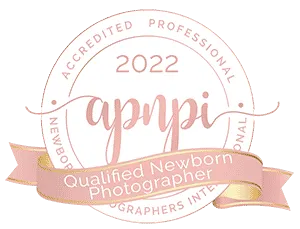 Circular badge with text "2022 APNPI Accredited Professional Newborn Photographers International" and a pink ribbon reading "Qualified Newborn Photographer.