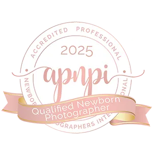 Circular badge featuring "2025 Accredited Professional Newborn Photographers International" and a pink ribbon that reads "Qualified Newborn Photographer," perfect for any Family Photographer Phoenix wanting to showcase their expertise.