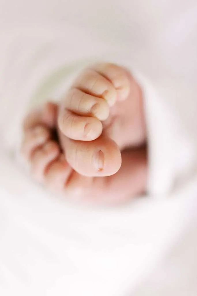 Close-up of a newborn baby's tiny toes and foot, wrapped in a soft white blanket—captured by a family photographer in Phoenix.