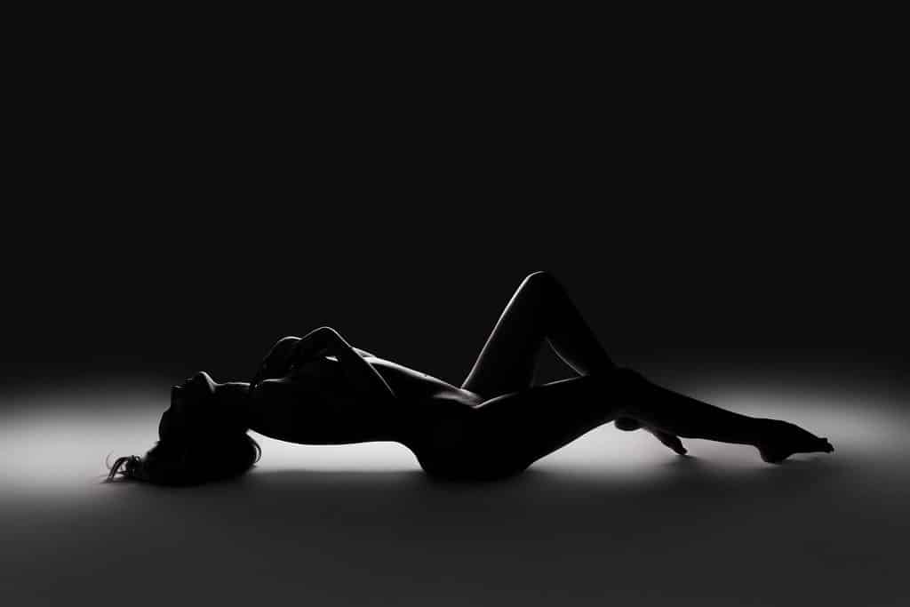 A person is lying on their back in a dark setting, with their body in silhouette against a soft white light on the floor.