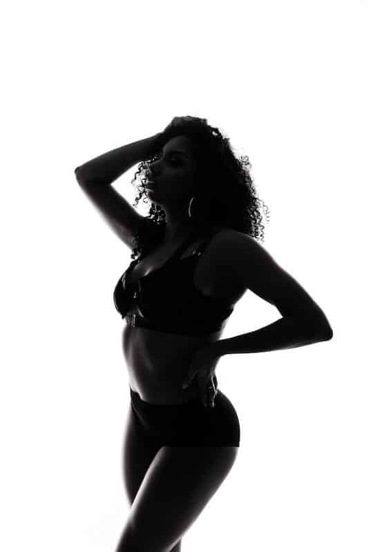 Silhouette of a woman with curly hair posing in lingerie against a white background.