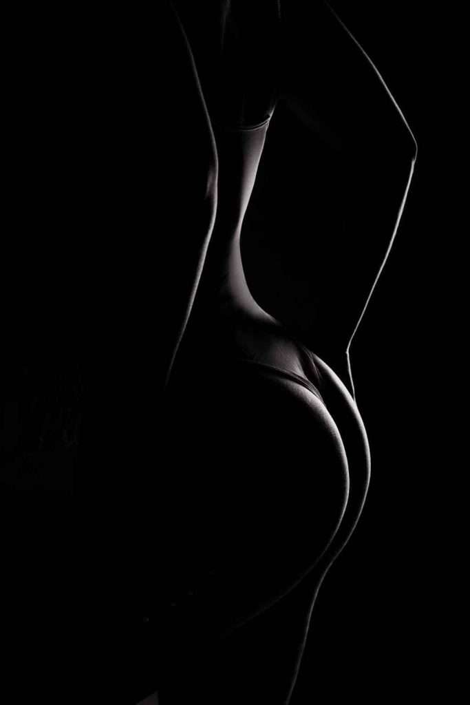 A silhouette of a person in underwear is shown from the back, with dramatic lighting highlighting the contours of their body against a dark background.