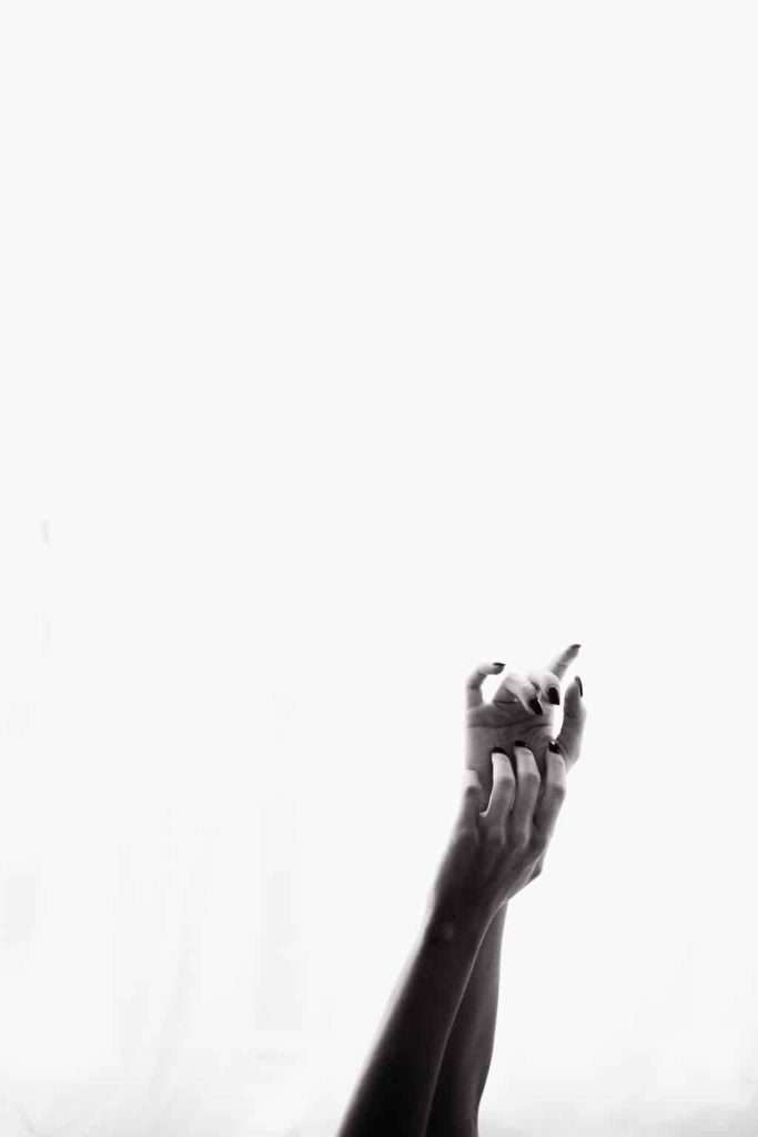 Two hands with intertwined fingers reach upward against a plain white background in a black and white photograph.