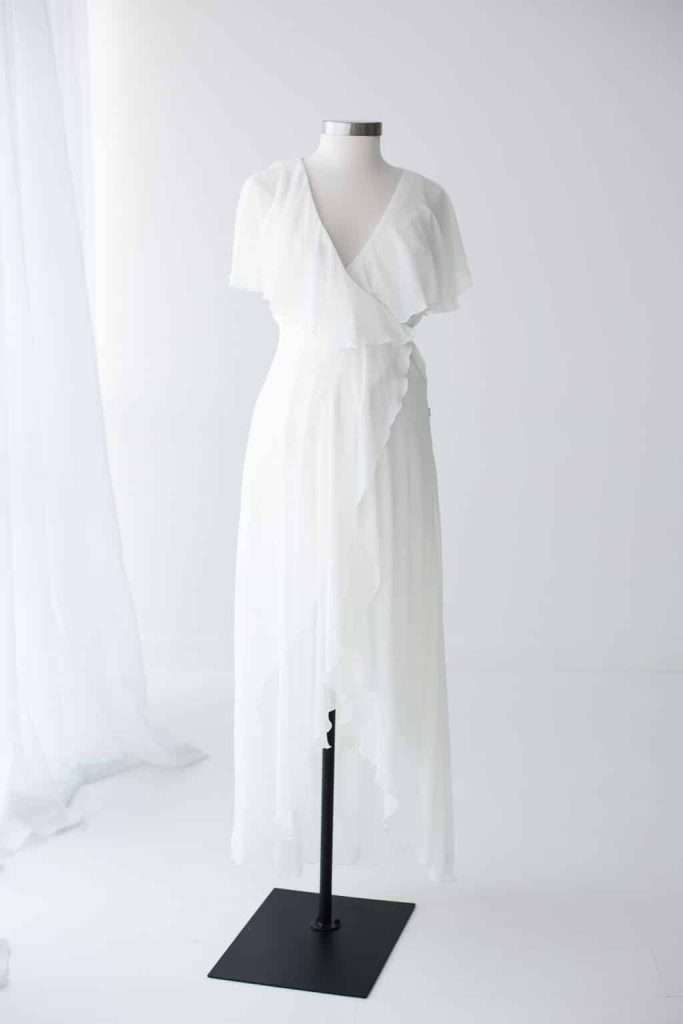 White wrap dress with short sleeves and an asymmetrical hem displayed on a mannequin against a plain, white background.