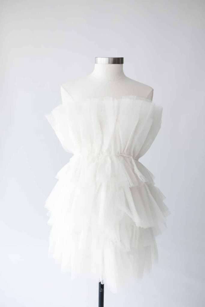 White strapless dress form with layered tulle ruffles is displayed on a mannequin against a plain light background.