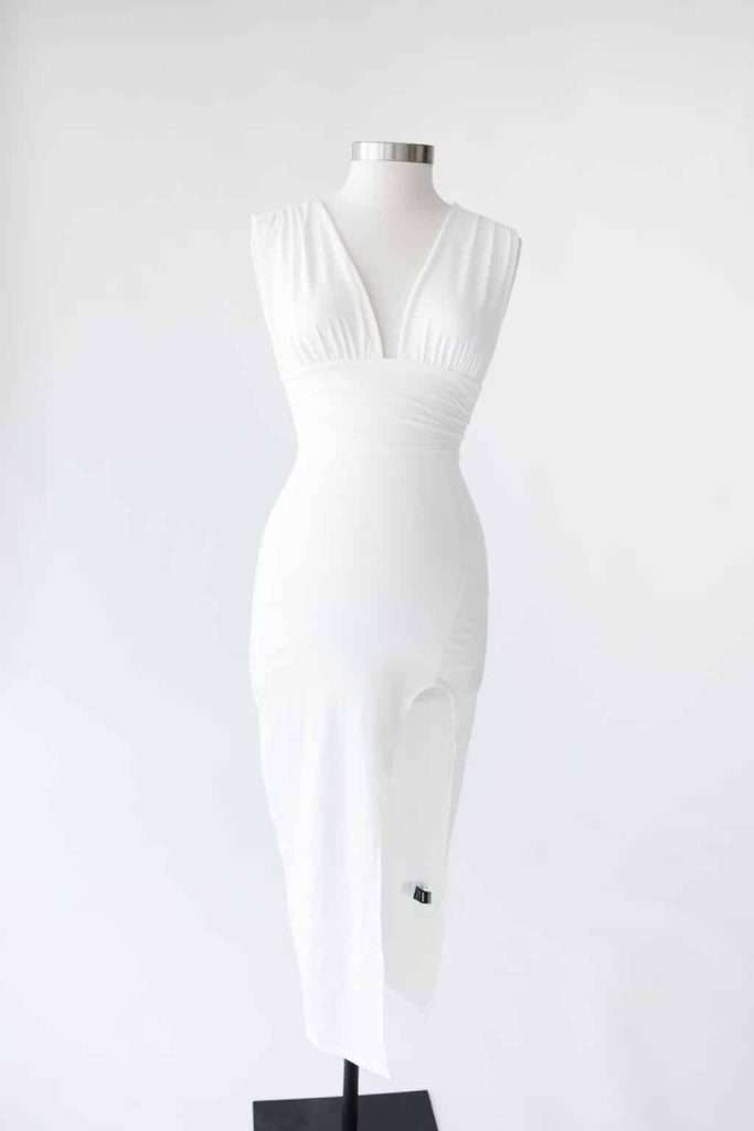 White sleeveless dress with a deep V-neck and thigh-high slit displayed on a dress form against a plain white background.