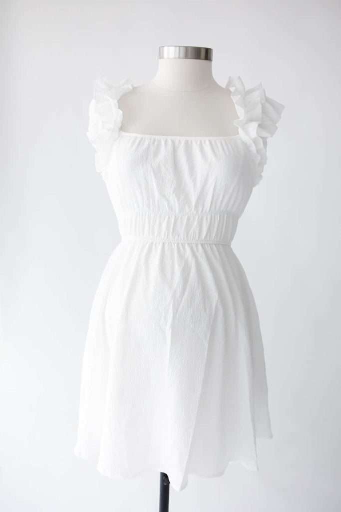 White sleeveless dress with ruffled shoulder straps displayed on a dress form against a plain white background.