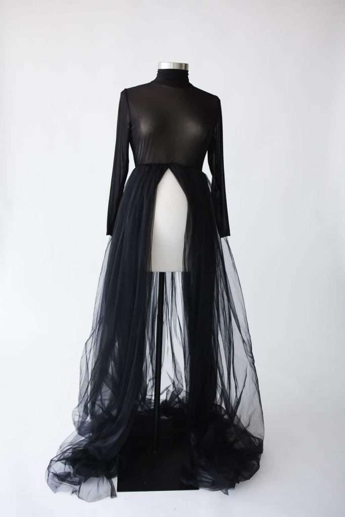 Black sheer maternity gown with long sleeves, a high neckline, and a flowing tulle skirt displayed on a dress form against a plain white background.