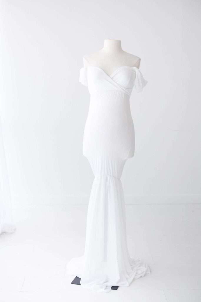 White off-the-shoulder, form-fitting gown with a long, flowing skirt displayed on a mannequin against a plain white background.