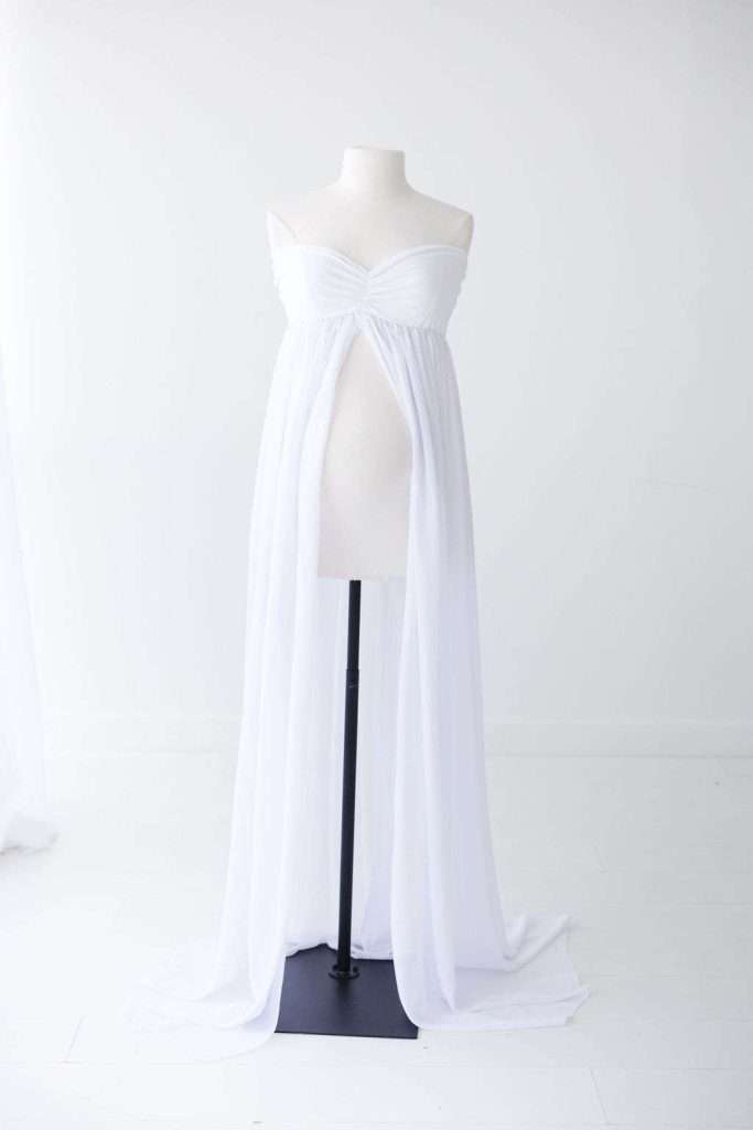 White strapless, floor-length maternity gown with a gathered bodice and a front slit, displayed on a dress form against a plain white background.