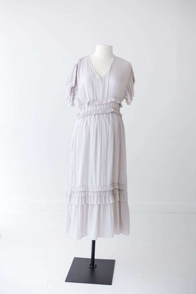 A light gray, short-sleeved, knee-length dress with ruffle details on sleeves, waist, and skirt, displayed on a white mannequin against a plain white background.
