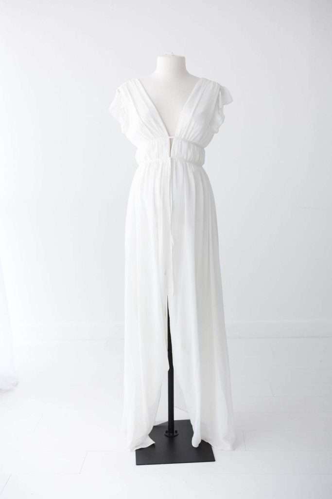 White, floor-length dress with a deep V-neckline, cap sleeves, gathered waist, and front slit, displayed on a dress form against a plain white background.