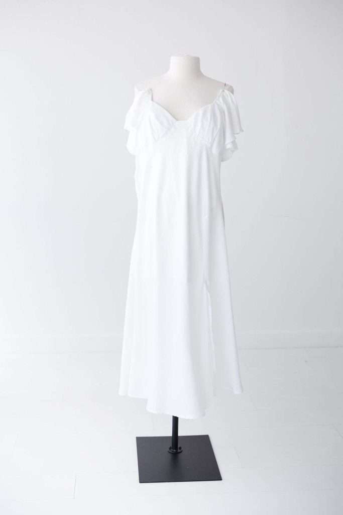 White off-shoulder, knee-length dress displayed on a mannequin in a plain, white, well-lit room.