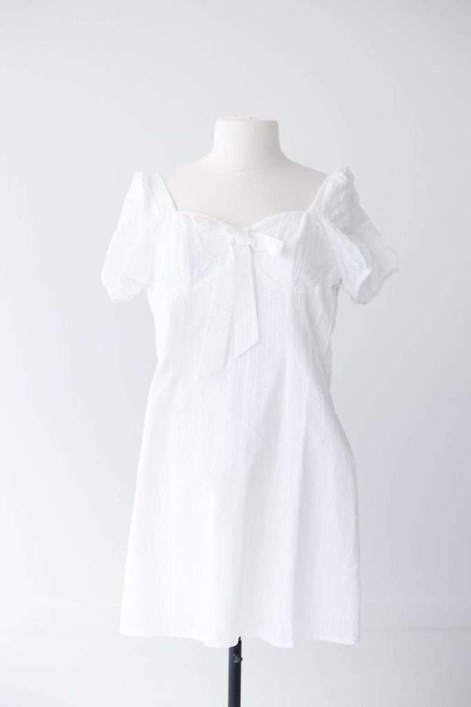 White short-sleeve dress with a bow on the chest, displayed on a mannequin against a plain light background.